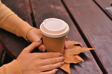 Paper glass of coffee in hand on the orange autumn leaves background