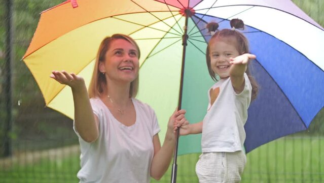 Young woman with a little daughter under a bright umbrella during a summer rain.