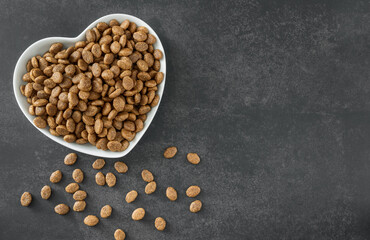 Dry cat food in a heart-shaped bowl on a dark background.