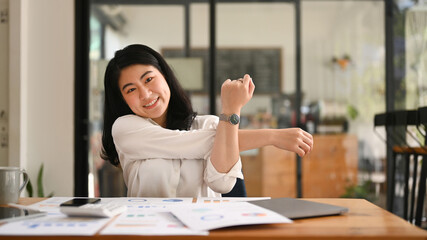 Happy female employee relaxing at work, reclining back in chair and stretching her arms