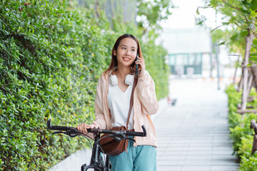 Fototapeta na wymiar Happy Asian young woman walking with bicycle using mobile phone in park, street city her smiling using bike of transportation, ECO friendly, People lifestyle concept..