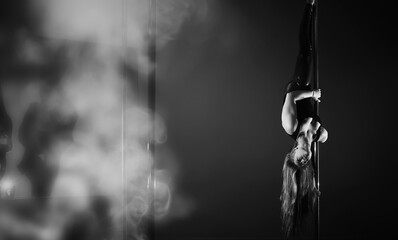 The dancer on the pylon in the studio. Girl doing exercises on a sports equipment.