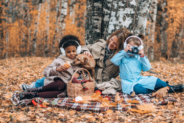 A multiracial family with a dog is having a picnic in the autumn park.Mother and two daughters...
