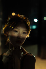 closeup vintage portrait of asian young woman with shadows on her face with blurred lights on the background