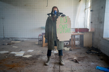 Fototapeta na wymiar Environmental pollution, ecological disaster, nuclear war, woman in gas mask with a banner that says: it's our future. Post apocalypse. Face-guard to prevent breathing toxic air.