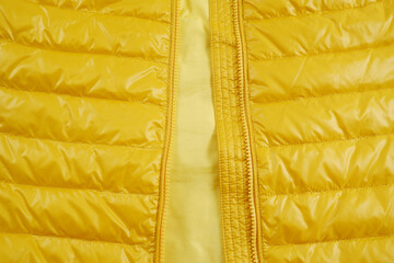 A bright background of a shortened-looking yellow down jacket with an unbuttoned zipper. Quilted jacket for autumn or winter with a large background. The concept of warm outerwear. View from above.