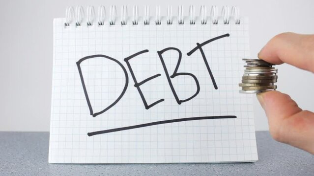 The word DEBT on a notepad and coins. The concept of DEBT. Collection, payment of debts.