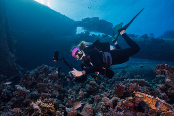 An underwater photographer looking at the camera taking pictures on the reef with a ship wreck in...