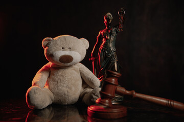 Judge gavel, figure of lady justice and teddy bear in a dark court room. Law and children concept