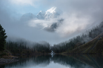 Tranquil scenery with snow castle in clouds. Mountain creek flows from forest hills into glacial...