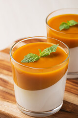 Close up coconut Panna cotta with mango sauce in glasses on white wooden table. Healthy dessert. Vegan food. Vertical orientation.