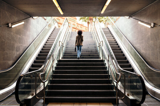 rear view of an unrecognizable business woman walking up the stairs of the subway station with a briefcase in her hand, concept of urban lifestyle and growth