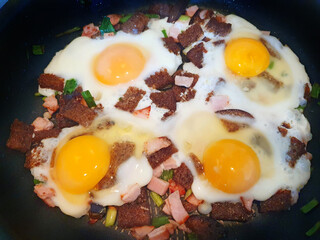 Scrambled eggs with rye croutons, ham, greens. Omelet in a frying pan of four chicken eggs