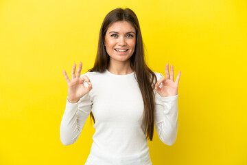 Young caucasian woman isolated on yellow background showing ok sign with two hands