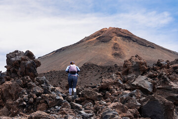 Fototapeta premium Woman with backpack on volcanic desert terrain. Hiking trail leading to summit volcano Pico del Teide, Mount Teide National Park, Tenerife, Canary Islands, Spain, Europe. Solidified lava, ash, pumice
