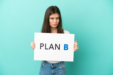 Young caucasian woman isolated on blue background holding a placard with the message PLAN B with sad expression