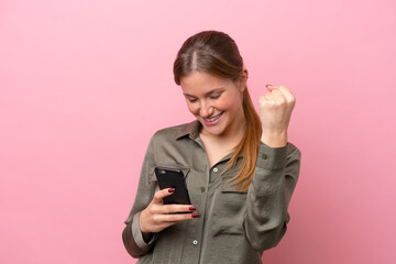 Young caucasian woman isolated on pink background with phone in victory position