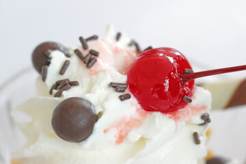 Close-up of a shiny bright red glace cherry on top of a sweet cream dessert 