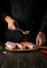 The chef adds paprika to raw meat ribs before grilling. Work environment on the kitchen table with spices and condiments