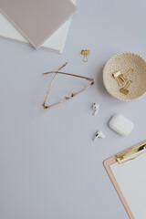 Flatlay of gold female accessories and office stuff. Comfortable home office workspace. Work at home. Clipboard, glasses, headphones, clips on table. Flat lay, top view