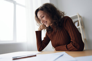 Cheerful happy smiling curly woman writing script counts taxes calculates budget for purchases...