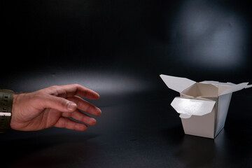 A man's hand picks up a package. Asian food: wok pasta, spaghetti, with vegatables in white box. black isolated. wooden chopsticks. Concept of production of paper containers for fast food.