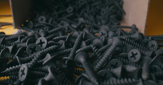 Super macro close up black screws on a orange background. Concept Screws for macro, Steel screws fall out of the box . Many screws lie together on a orange table.
