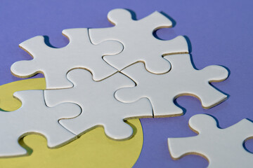 Close-up on jigsaw puzzle pieces, blank white paper jigsaw puzzle elements linked together and separate. Closeup shot on yellow and purple paper. Abstract background metaphor on teamwork challenge.