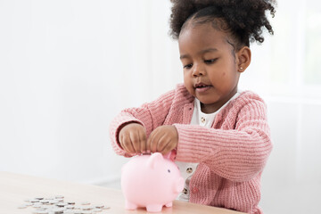 Child girl kid putting money into the piggybank. African American girl kid inserting a coin in a...