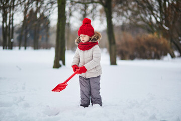 Adorable preschooler girl having fun in beautiful winter park on a snowy cold winter day