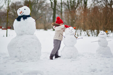 Adorable preschooler girl building a snowman on a day with heavy snowfall
