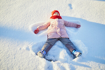 Fototapeta na wymiar Adorable preschooler girl having fun in beautiful winter park on a snowy cold winter day