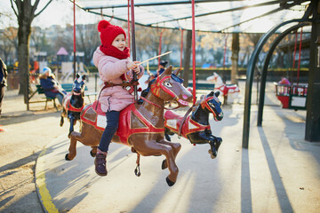 Adorable preschooler girl riding a horse on merry-go-round on Christmas market in Paris