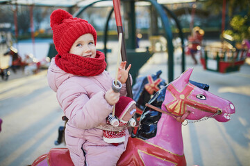 Adorable preschooler girl riding a horse on merry-go-round on Christmas market in Paris