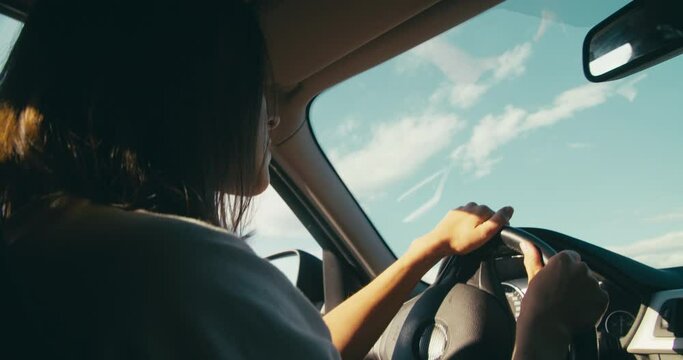 Young adult woman on summertime vacation road trip driving a car. Female traveler in slow motion low angle footage drives vehicle on journey adventure. 