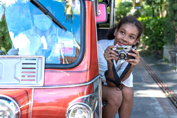 Young hipster traveller woman holding camera sitting in tuktuk local taxi sightseeing Chiang mai,...