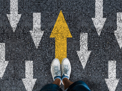 man sneakers on asphalt and opposing direction arrows on asphalt ground, personal perspective footsie concept for finding your own way
