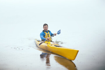 Fototapeta na wymiar One man paddling kayak at autumn misty river at foggy autumn morning.