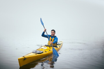 One man paddling kayak at autumn misty river at foggy autumn morning.
