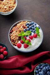 Yogurt with granola and berries in bowl. Composition with healthy breakfast and ingredients with burgundy napkin. Flat lay