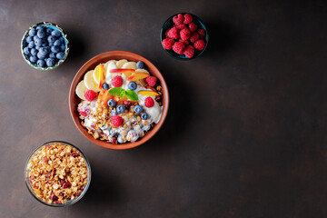 Yogurt with granola, berries, fruits and fresh mint. Plate with a healthy breakfast and ingredients on a dark background. Top view. Copy space