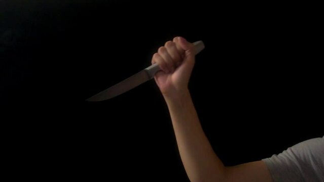 Human hand with knife shot on black background. Woman's hand holds knife. The hand makes stabs with a knife. Concept of violence, murder with kitchen knife