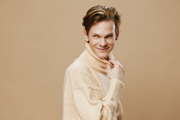 a pleasant, funny guy in a beige, autumn sweater poses pulling back his neck while standing on a...