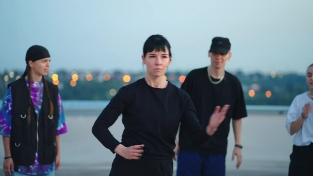 young woman is dancing robot dance, party of street style dancers on roof, portrait of emotionless lady
