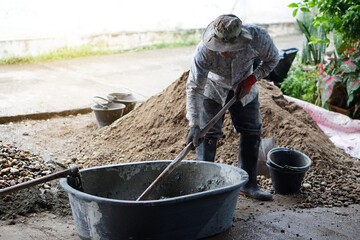 Man worker manually works at construction site,  Using a hoe to mix cement powder, sand, stones in...