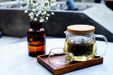 A teapot or teko equipped with tea infuser was beside a blurry artificial flower. It was half-filled with oolong tea and ready to pour into a cup