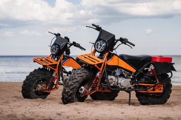 Two custom off-road sports motorcycles are parked on the beach outdoors © alexkoral