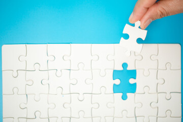 Close up hand holding and playing jigsaw game incomplete. White part of jigsaw puzzle pieces on blue background. concepts of problem solving, business, teamwork.