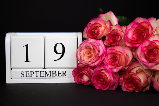 September 19 wooden calendar, white on a black background, pink roses lie nearby.Postcard with copy space. The concept of a holiday, congratulation, invitation, party, announcement, vacation,promotion