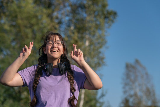 happy smiling teenage girl with headphones around her neck made a wish and crossed her fingers for good luck